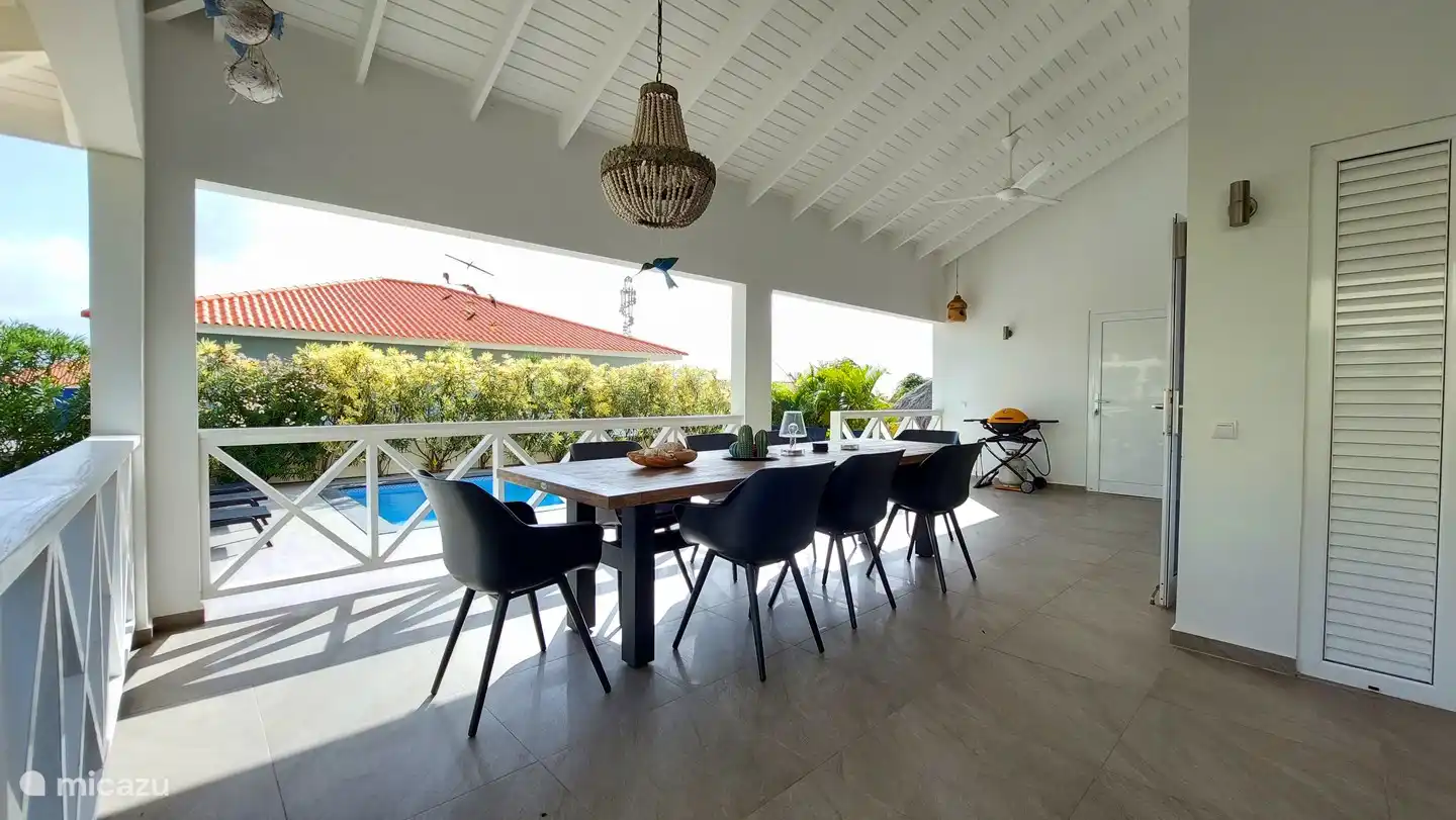 El juego de comedor en el porche. El conjunto se compone de 8 cómodas sillas y una mesa de teca de 3x1m. Es agradable desayunar, almorzar y cenar aquí. En Curacao vives principalmente en el exterior, es agradable quedarse en el porche de esquina de 42m2. El porche tiene 2 ventiladores de techo para refrescarse