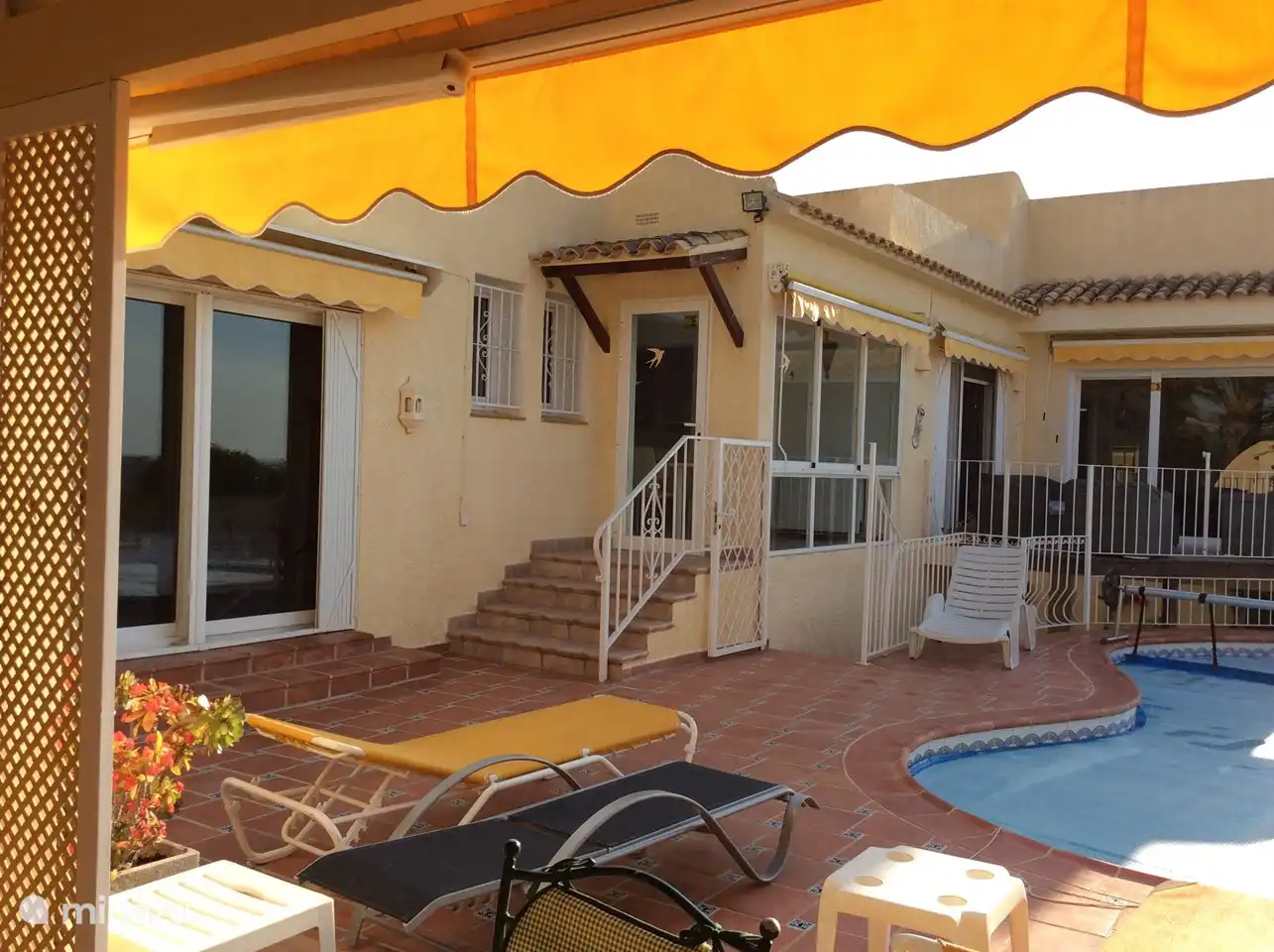 Links das braune Zimmer, Treppe hinauf zur Küche und zum Esszimmer, rechts Terrasse mit Lounge-Set und dahinter das graue Zimmer