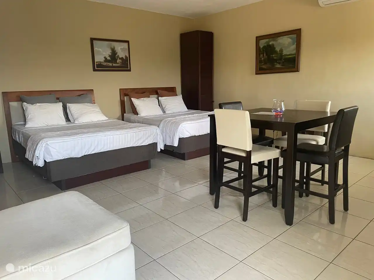 Hier sieht man 2 Doppelbetten nebeneinander und den Esstisch in der Mitte des Raumes. 