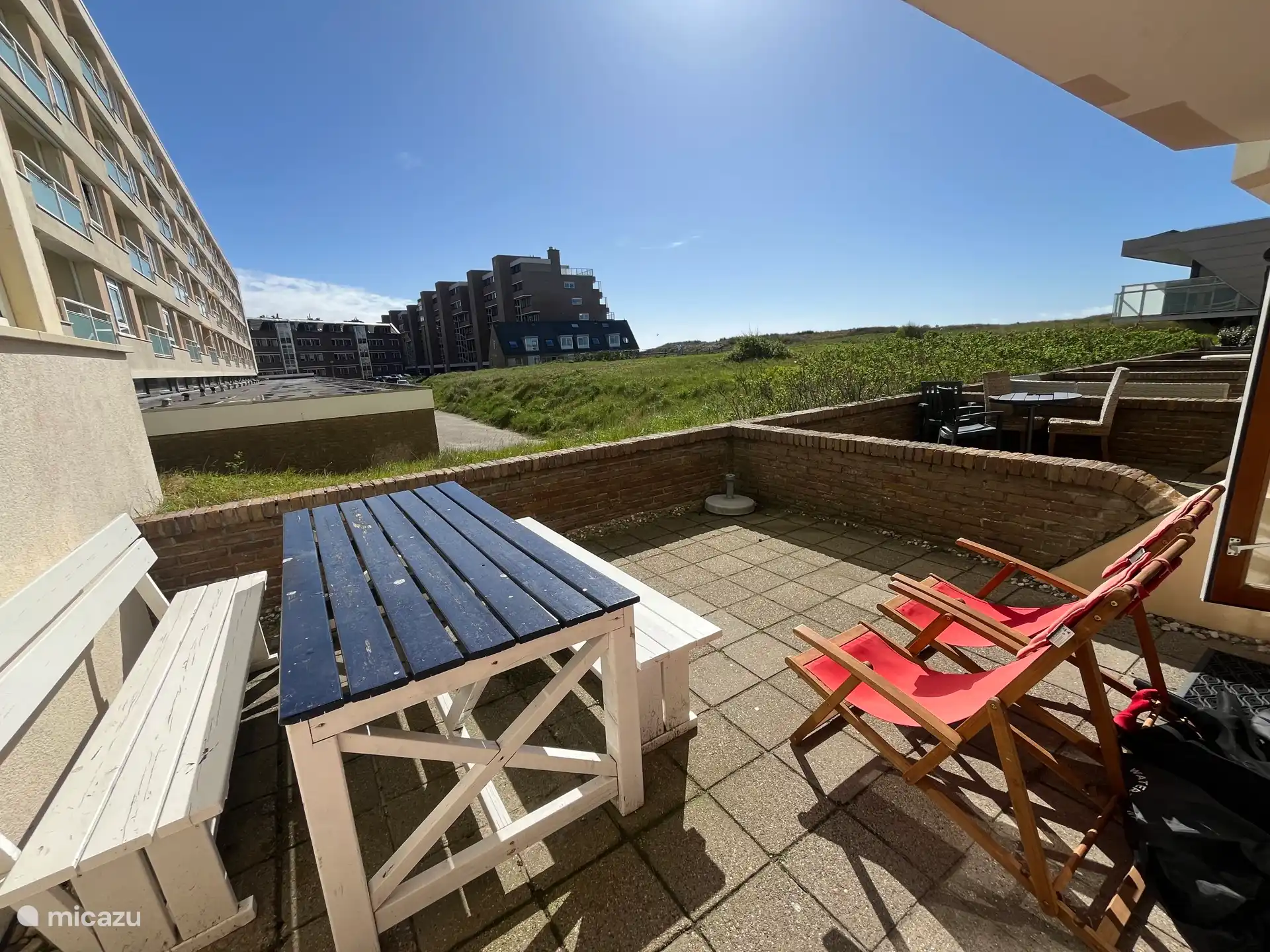 Zonnig en beschut terras met grote eettafel en ligstoelen