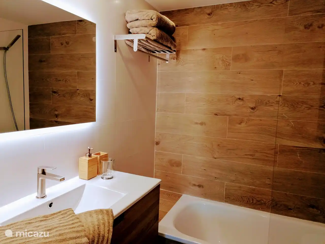 De wit met houten badkamer met bad waarin ook een douche, wastafelcombinatie en toilet en bidet.