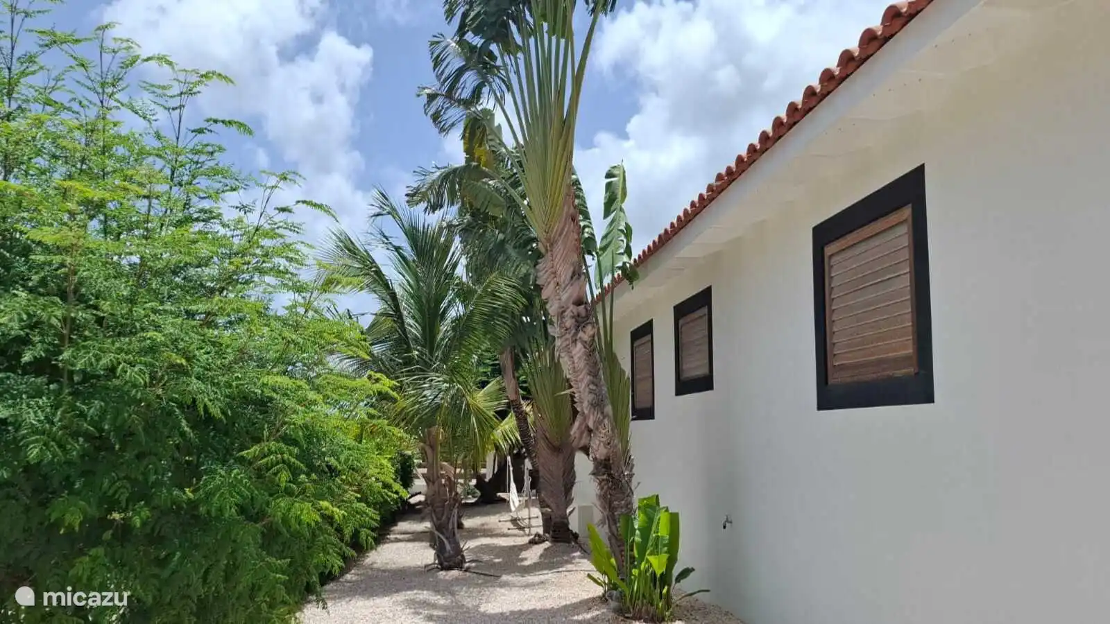 Avec sa superficie totale de 755 m2 de terrain, la villa dispose d’un jardin tropical spacieux et magnifiquement aménagé et de plusieurs terrasses. Ici, vous pouvez voir une vue latérale du jardin.