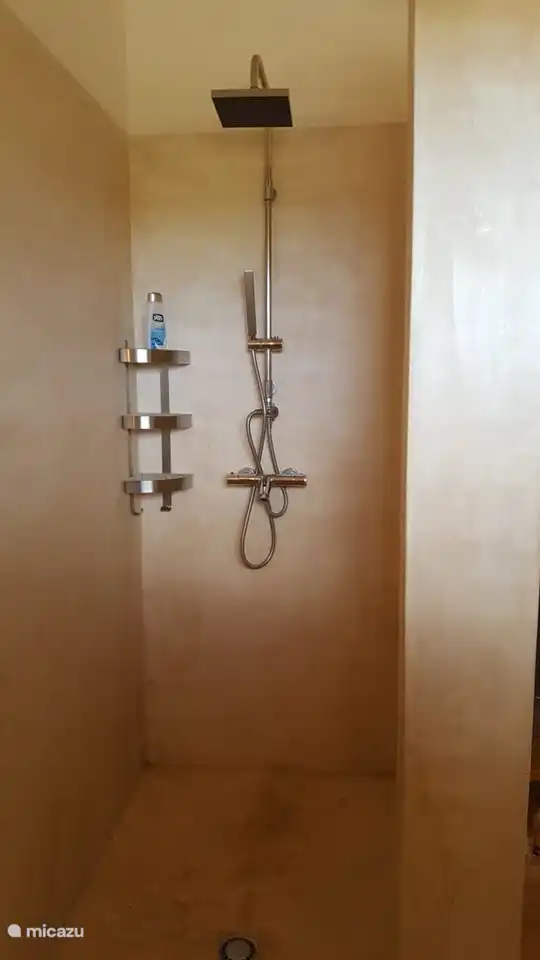 La salle de bain attenante est équipée d'un grand espace douche ouvert, équipé d'un mitigeur thermostatique, d'une douchette et d'une douche à effet pluie