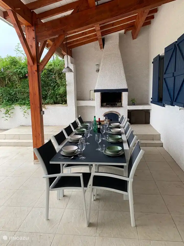 Tisch im Freien unter überdachter Veranda mit dahinter dem Außenkamin, in dem Sie auf einem Grill grillen können. 