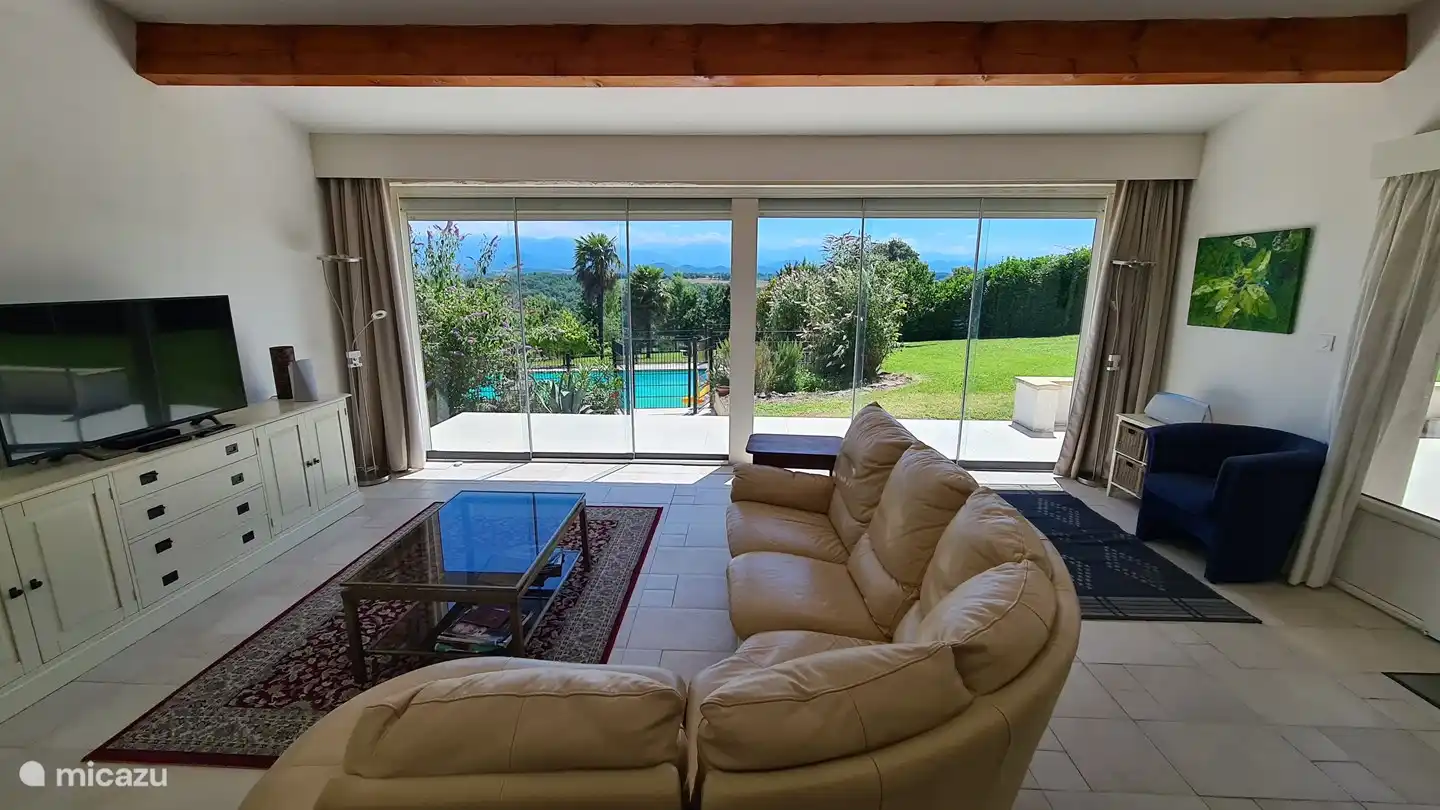 Wohnzimmer mit Blick auf den Garten und den Pool im Sommer. Die Glasschiebetüren können eingefahren werden, so dass 2 der 3 Paneele eingefahren sind. Dies kann beidseitig erfolgen. Das bietet einfachen Zugang zu Schwimmbad, Whirlpool und Garten. Halten Sie Ausschau nach Fliegen und anderen Tieren. 