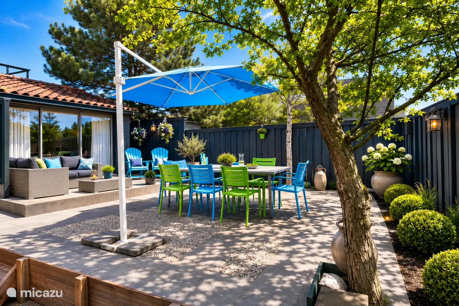 Een zonnig zomerterras met een loungehoek, een eettafel voor 7 personen en een blauwe parasol. Geniet van luie middagen of warme zomeravonden, gewoon hier in huis!