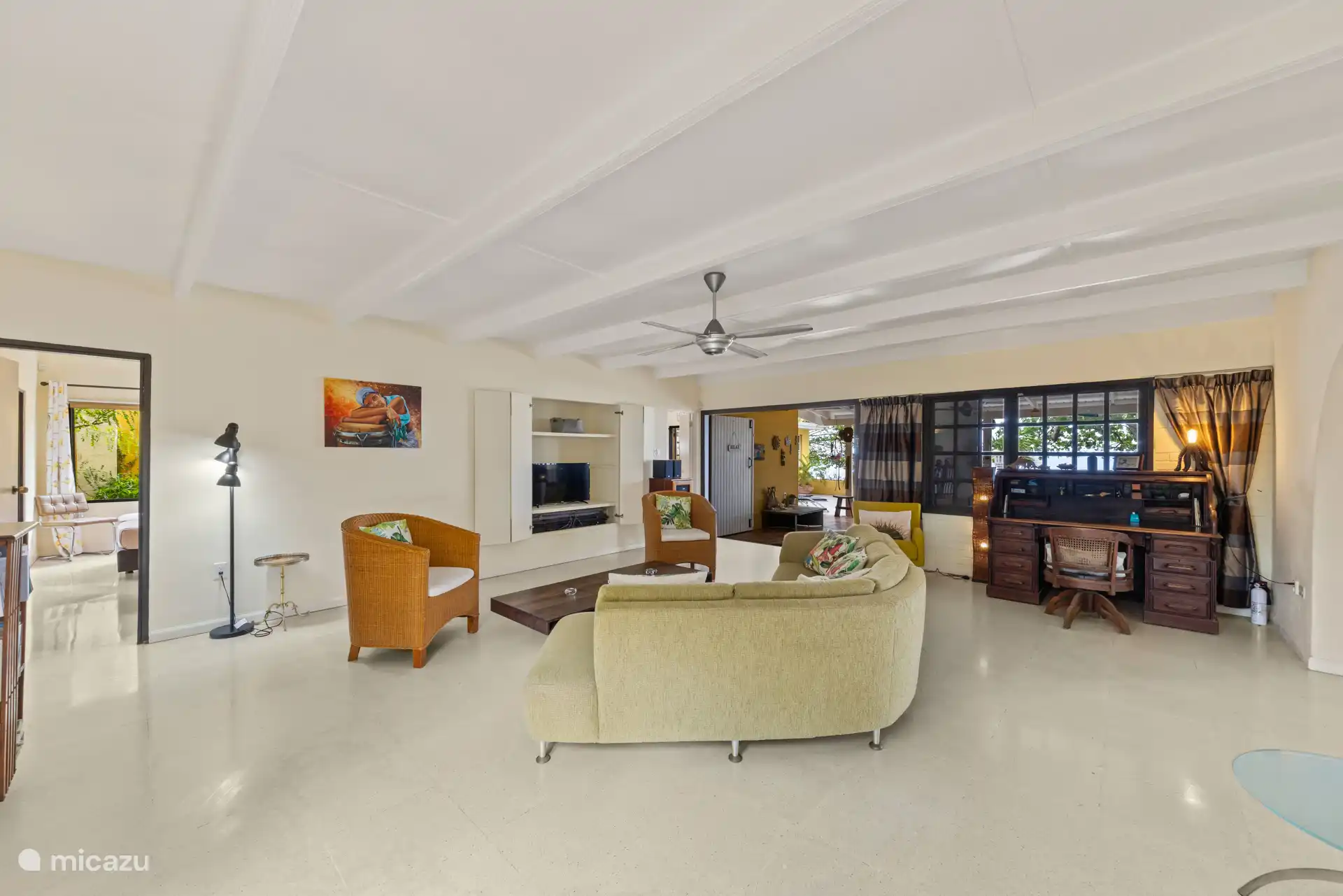 Sehr geräumiges Wohnzimmer mit Arbeitsplatz. Fernseher und Fan anwesend.