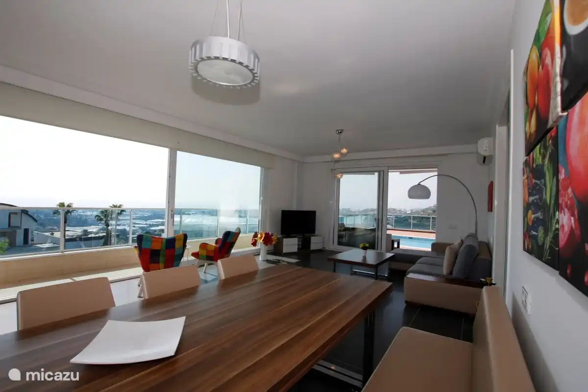 Blick auf das Wohnzimmer mit großem Fernseher in der Ecke und Meerblick durch alle Fenster