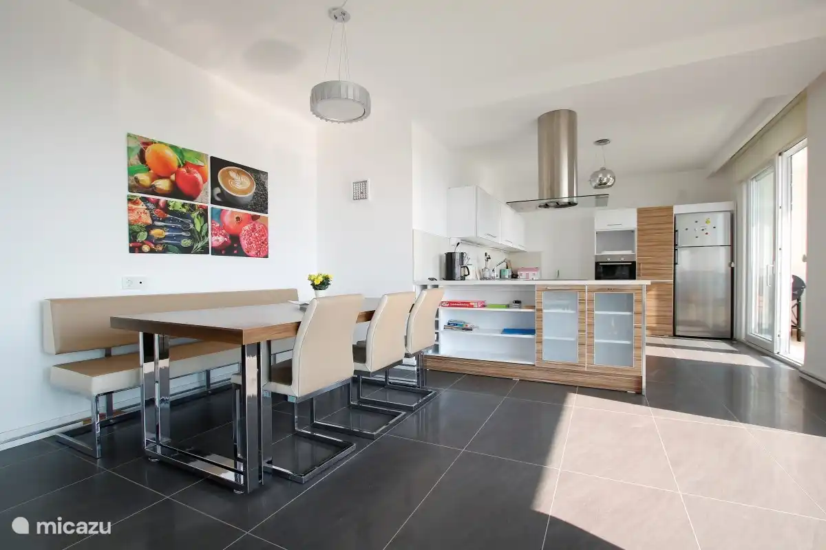 Essbereich mit dahinter liegender moderner Küche mit Kühlschrank und Kühlschrank, Geschirrspüler, Backofen, Kaffeemaschine, Wasserkocher, Elektroherd und Inventar
