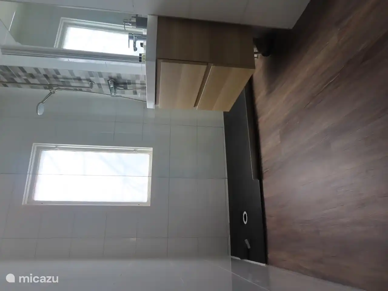 Ein geräumiges Badezimmer mit ebenerdiger Dusche, Waschbecken und Toilette. Der Raum wird mit einer Infrarotplatte beheizt.