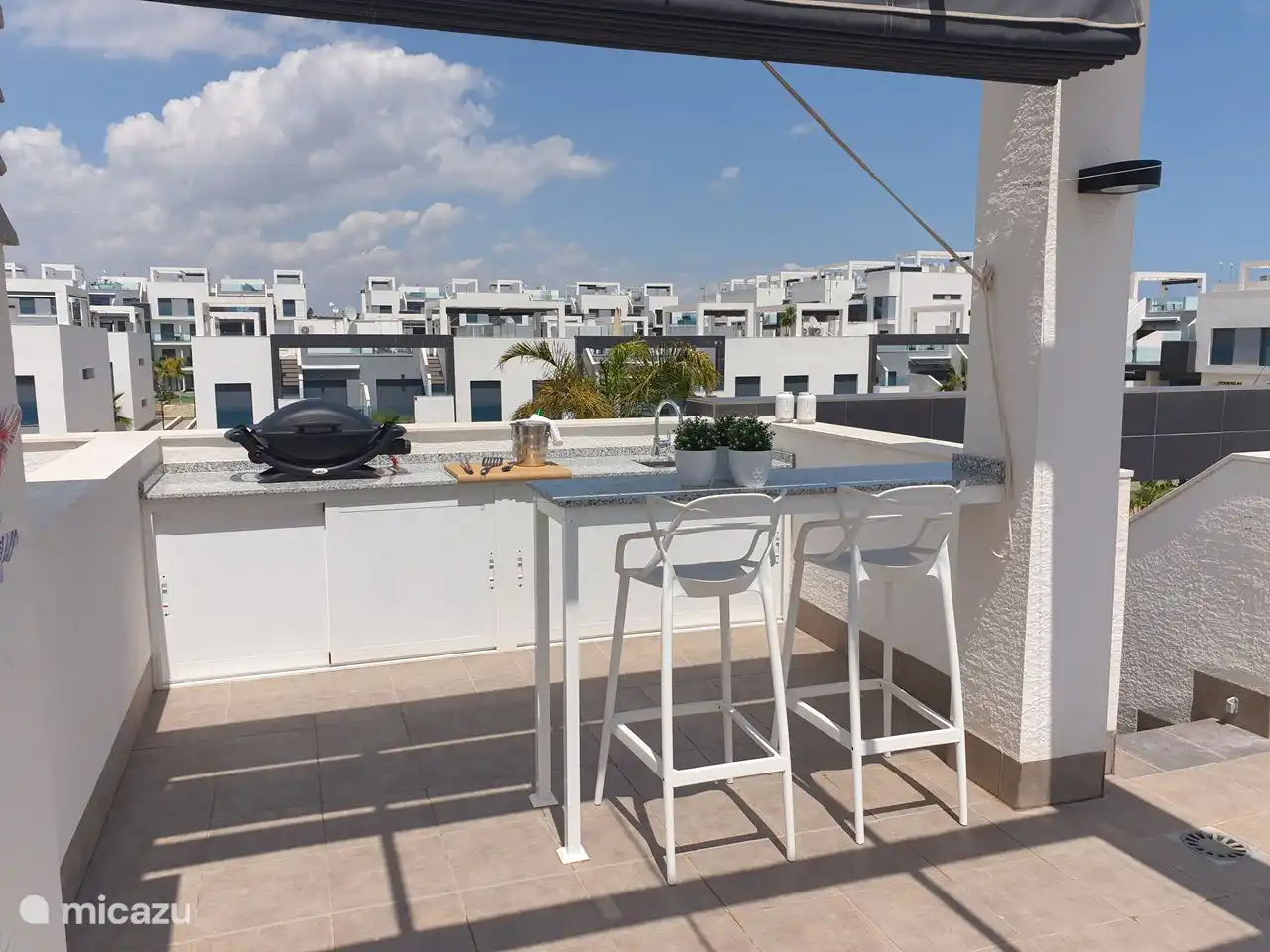 La terraza de la azotea de 70 m2 está equipada con una cocina exterior con barbacoa de gas y fregadero, una barra alta con 2 taburetes, un comedor para 4 personas que incluye toldos horizontales, 2 tumbonas con cojines de sol de lujo, una cómoda sala de estar con un sofá para 2 personas y 2 sillones separados. Ducha exterior con agua caliente.