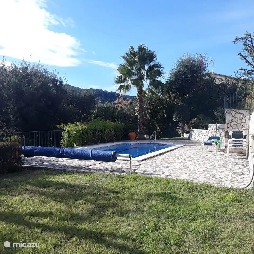 Private swimming pool surrounded by a paved area and a lawn, with adjoining garden house with toilet.