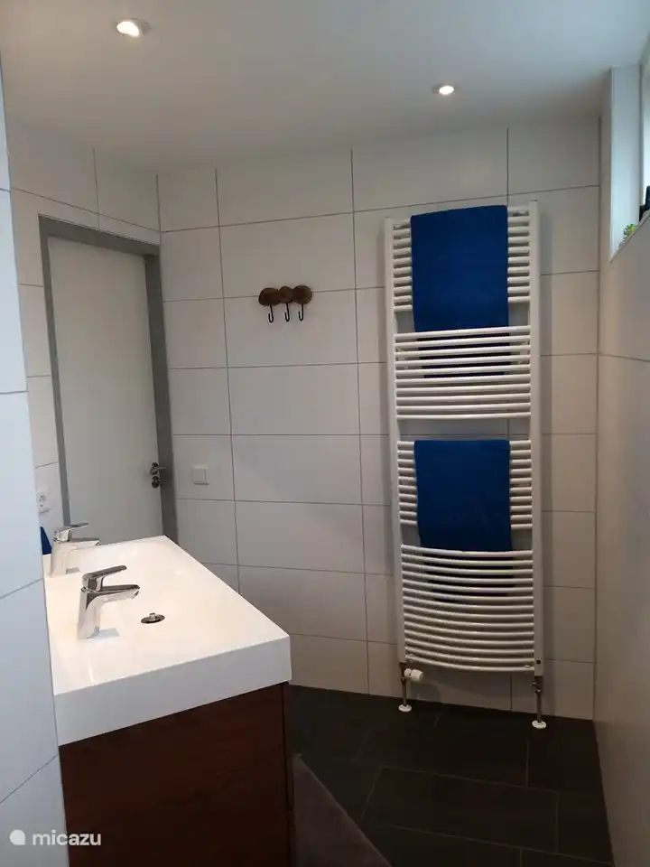 Das Badezimmer mit ebenerdiger Dusche, Doppelwaschbecken und Handtuchheizkörper.