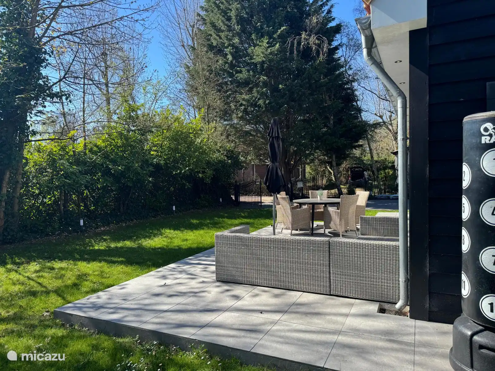 Sonnige Terrasse mit Loungebereich und Esstisch, ideal zum Entspannen oder Essen im Freien. Umgeben von viel Grün und schattenspendenden Bäumen für einen wunderbar privaten und erholsamen Aufenthalt.