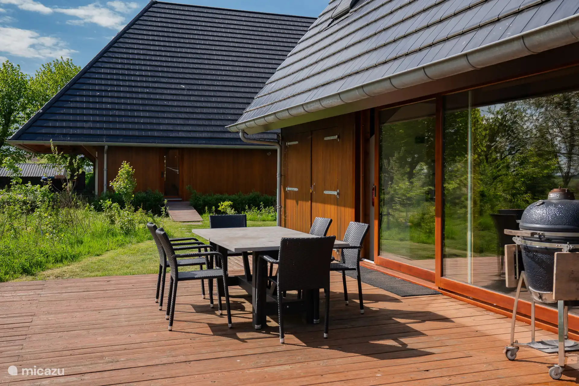 Encantadora terraza espaciosa con mesa de jardín y una gran barbacoa Kamado Takumi.