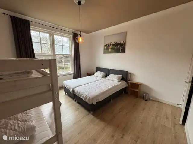 Granja de vacaciones De Steeg en Países Bajos, Güeldres, De Steeg - casa de campo La habitación para 4 personas con una litera y dos camas individuales. Si miras por la ventana tienes una vista de una de las dos terrazas que tiene la casa rural.