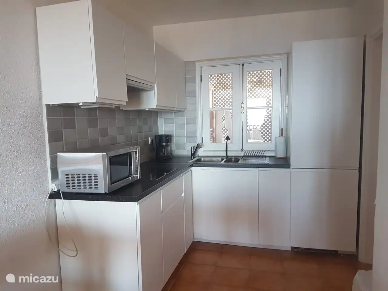 Cuisine avec fenêtre extérieure donnant sur la 1ère salle. Plaque d’induction avec extracteur au-dessus