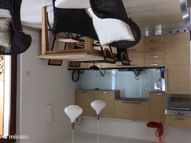 kitchen with refrigerator, combi-oven, dishwasher and cooking area (gas). dining table with modern chairs. on the right the patio doors to the terrace.