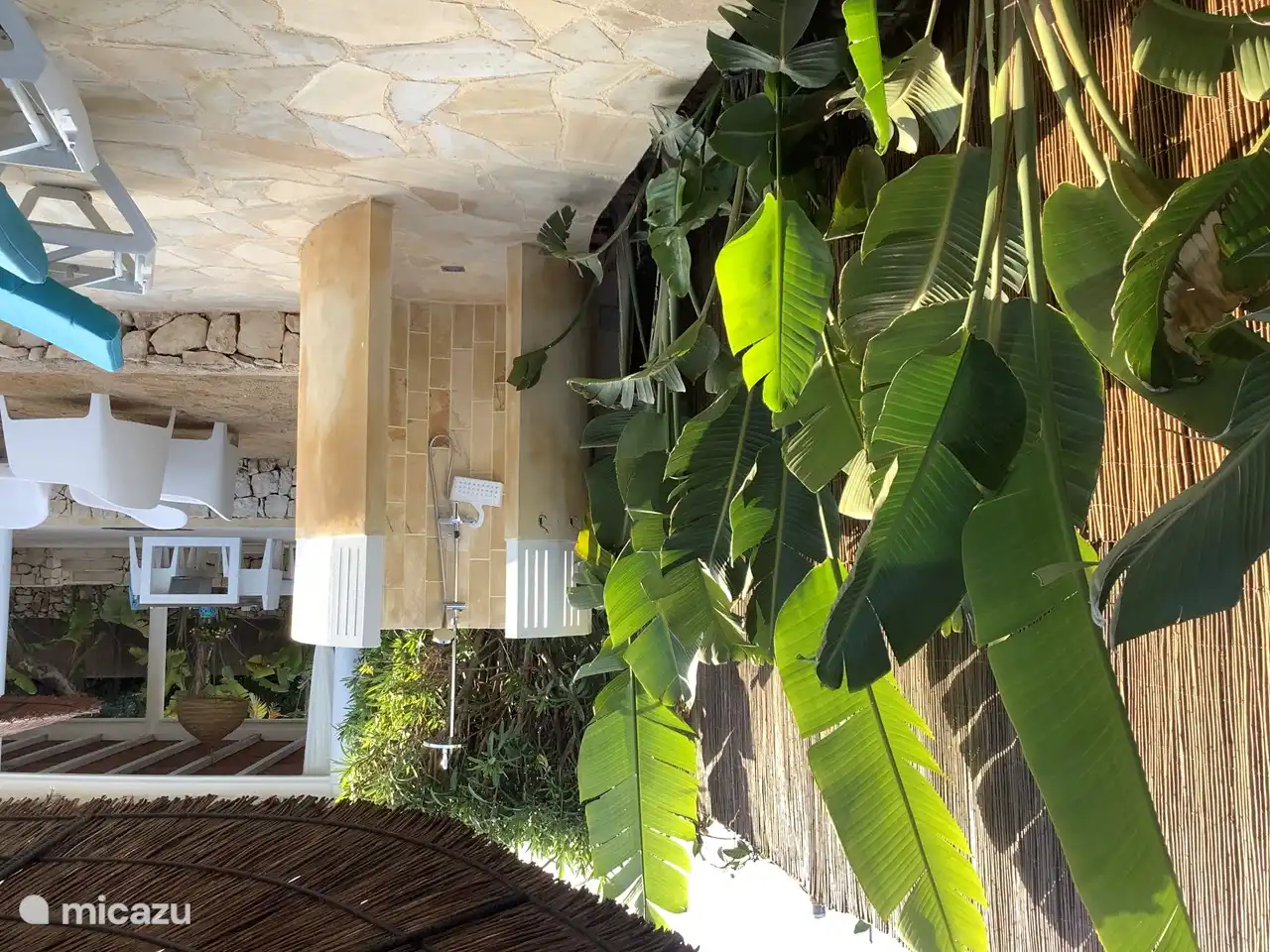 Außendusche mit heißem Wasser, umgeben von tropischen Pflanzen.