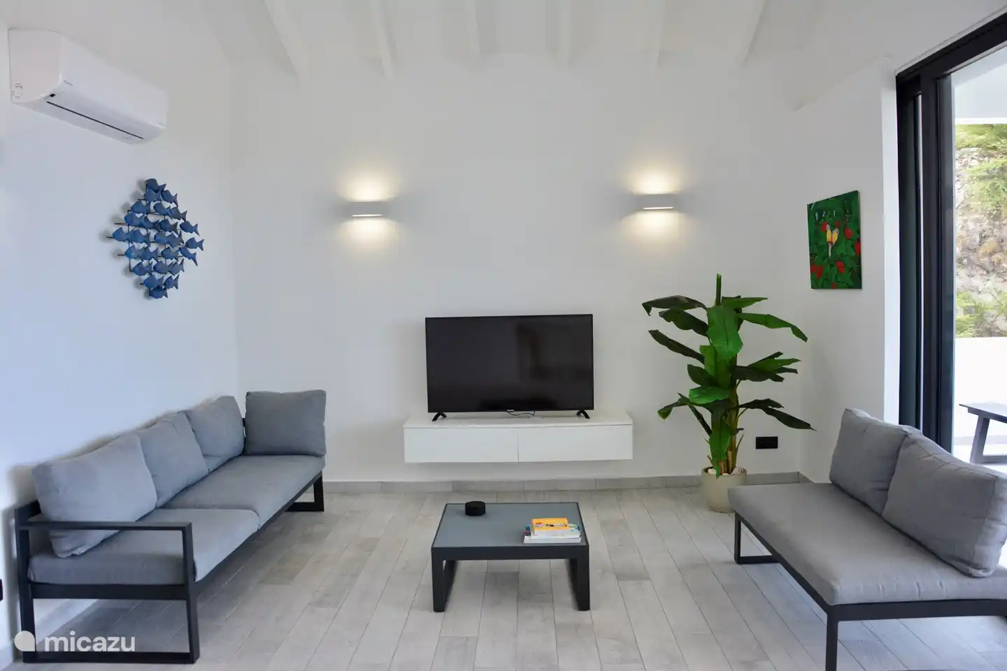 Wohnzimmer mit Smart TV und über 50 Kanälen, Klimaanlage und Schiebetüren zur 30 m² großen Terrasse. An den Wänden lokale Kunst