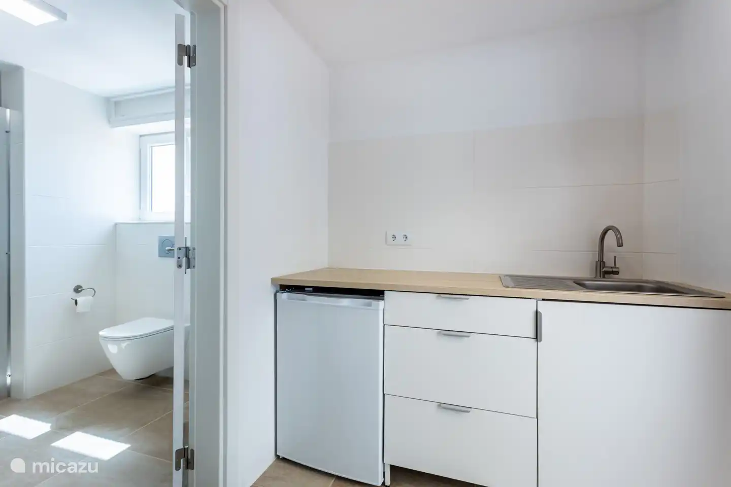 Pequeña cocina con acceso a baño con inodoro.