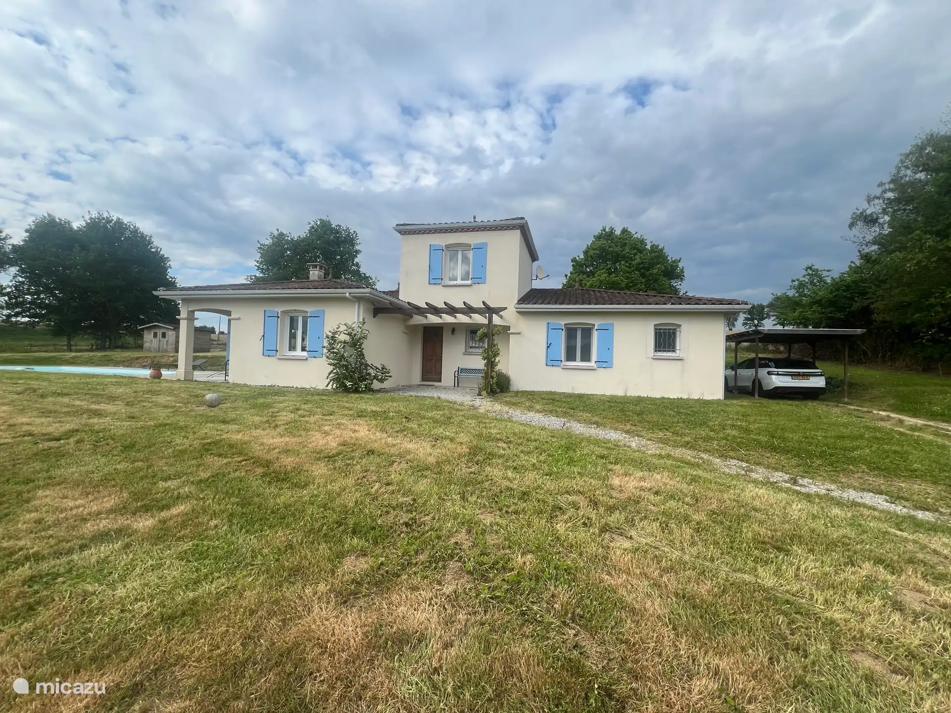 Vorderansicht des Bungalows mit dem Pool auf der linken Seite und dem Carport auf der rechten Seite.