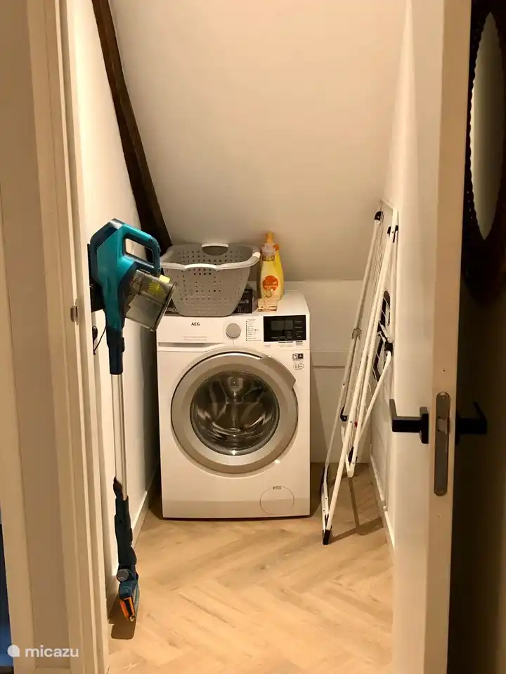 Abstellraum mit Waschmaschine, Staubsauger, Wäscheständer, Bügelbrett und Bügeleisen.