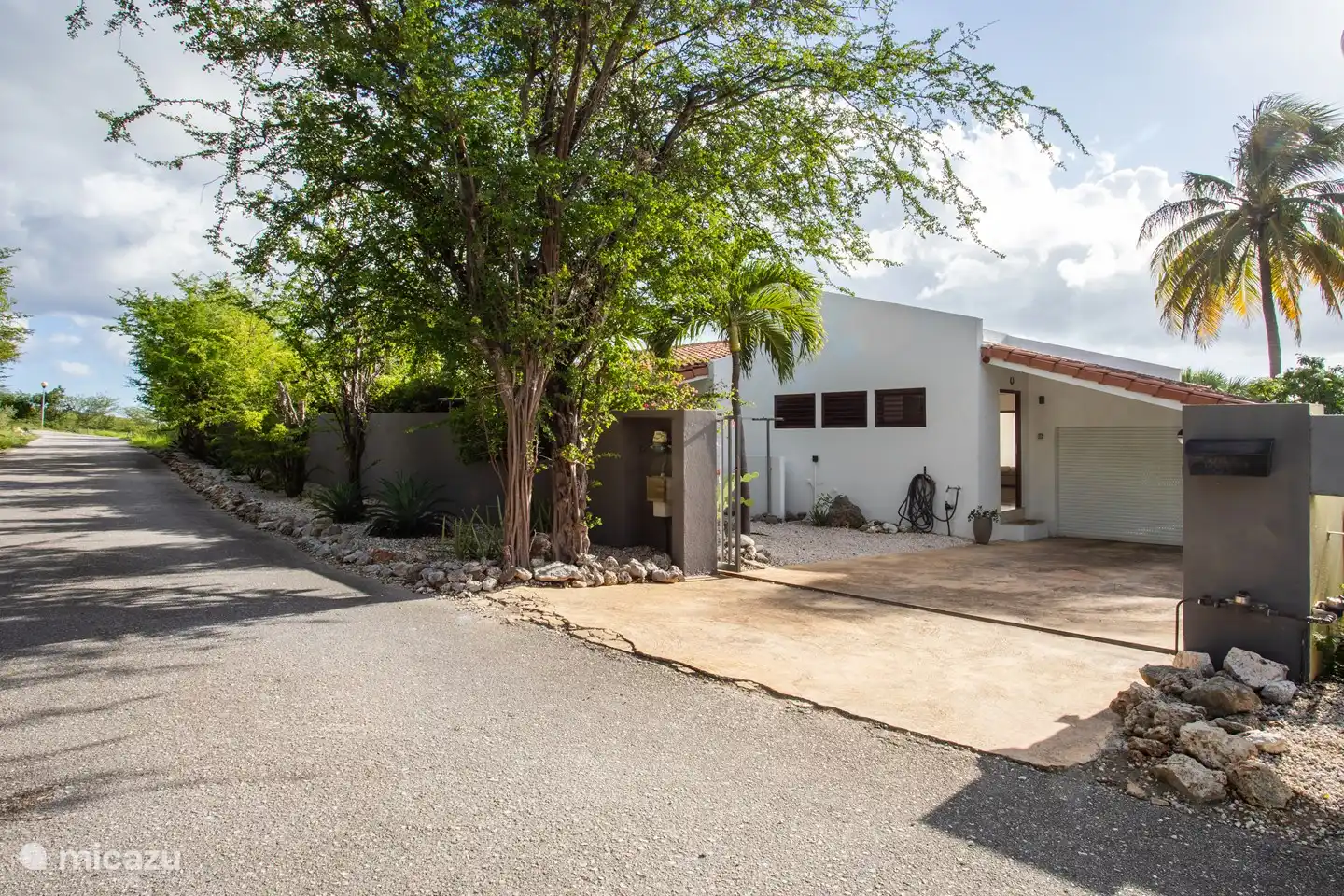 Vorderansicht der Villa mit Parkplatz hinter dem Zaun.