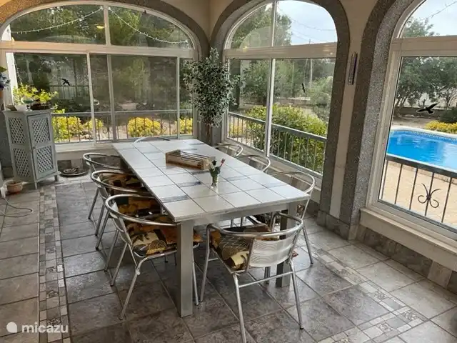 Vom großzügigen Wintergarten in Wohnung 1 haben Sie einen Blick auf den Garten und das Schwimmbad. In der Wintersaison ist der nach Südosten ausgerichtete Wintergarten ein angenehmer und sonniger Platz in der Wohnung. Es gibt einen großen Esstisch mit 8 Stühlen.