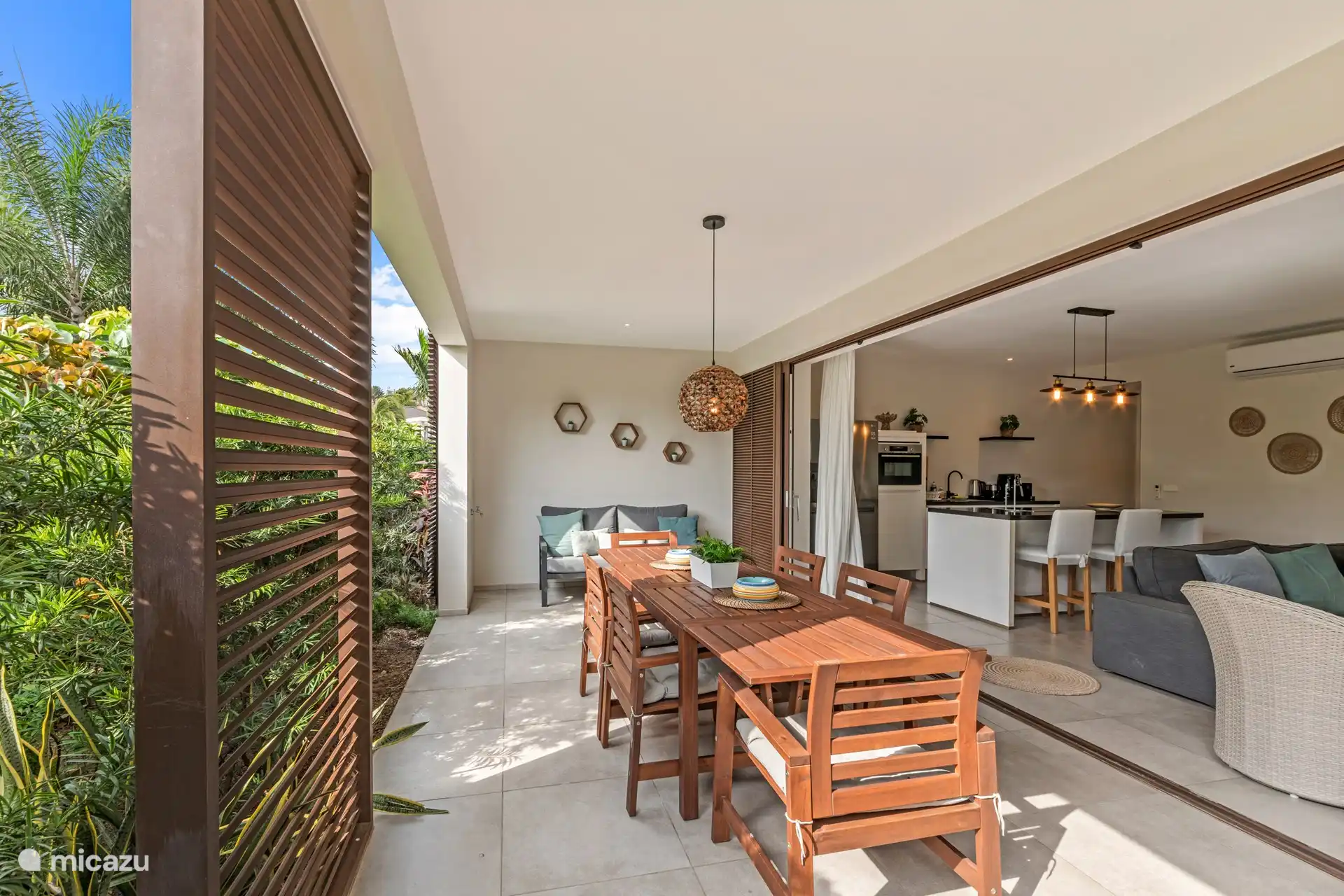 Terrasse ombragée avec grande table à manger et coin salon confortable.