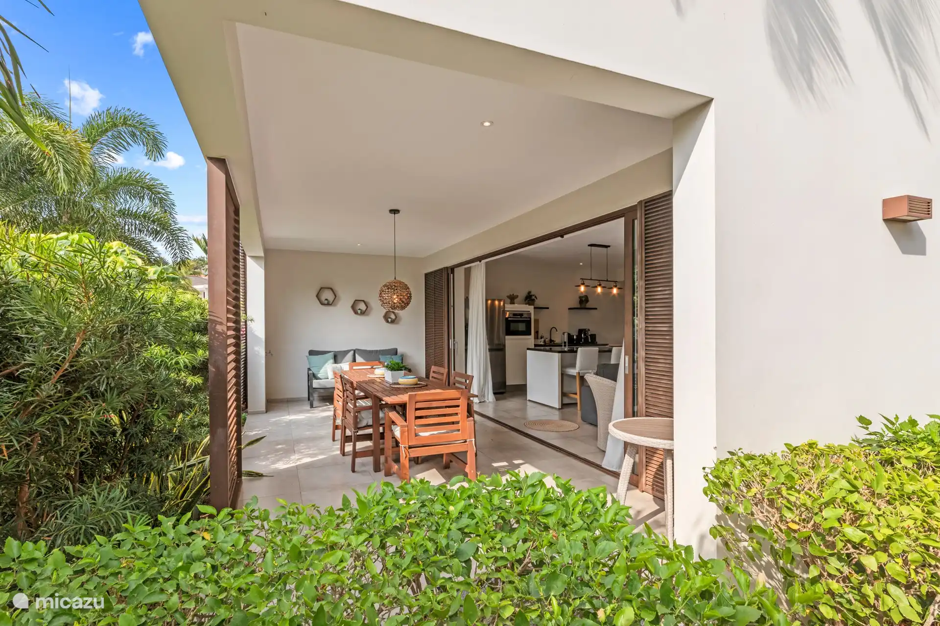 Terrasse ombragée avec grande table à manger et coin salon confortable.