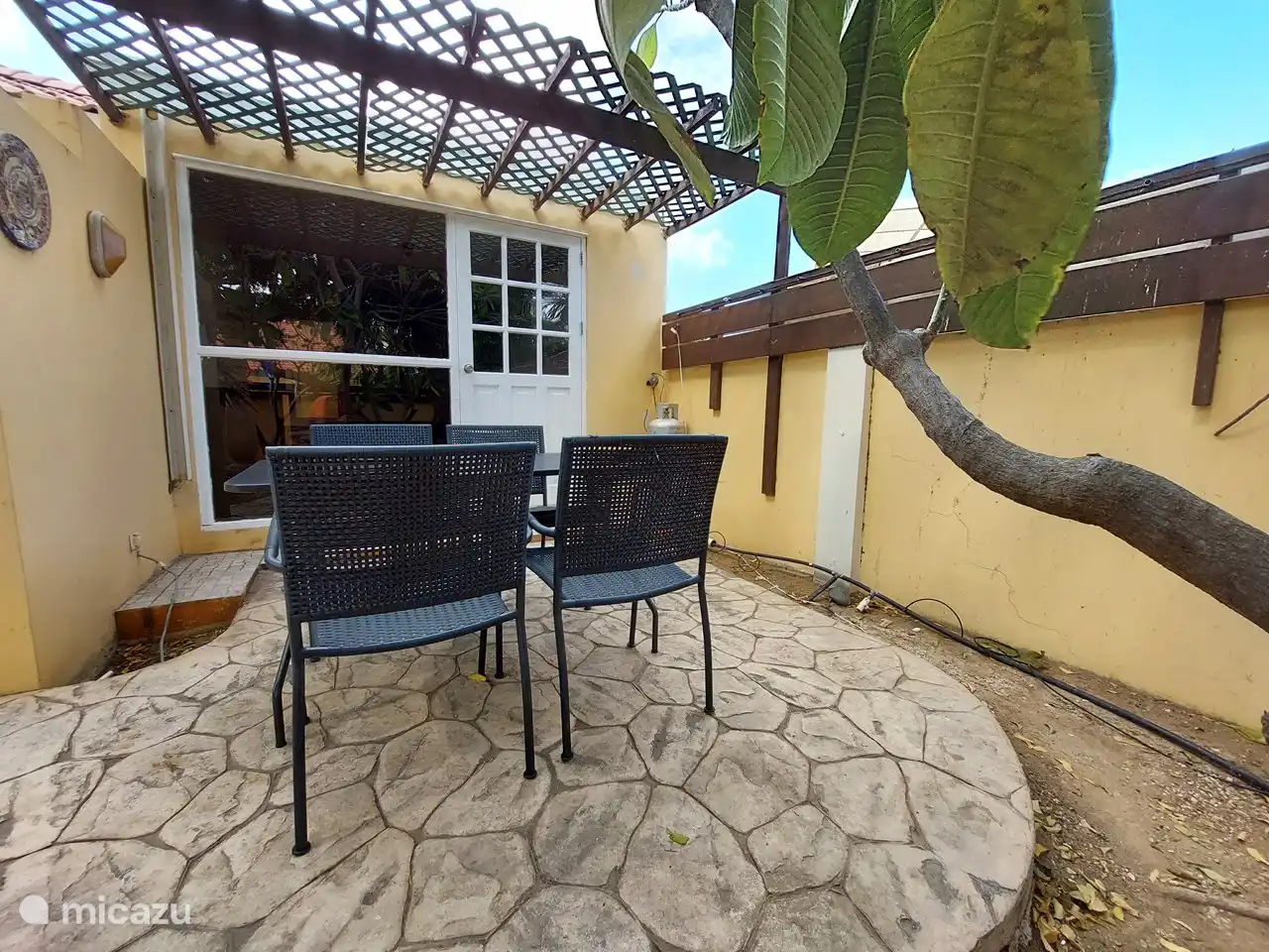 Zona de estar al aire libre con mesa y 4 sillas con sombra.