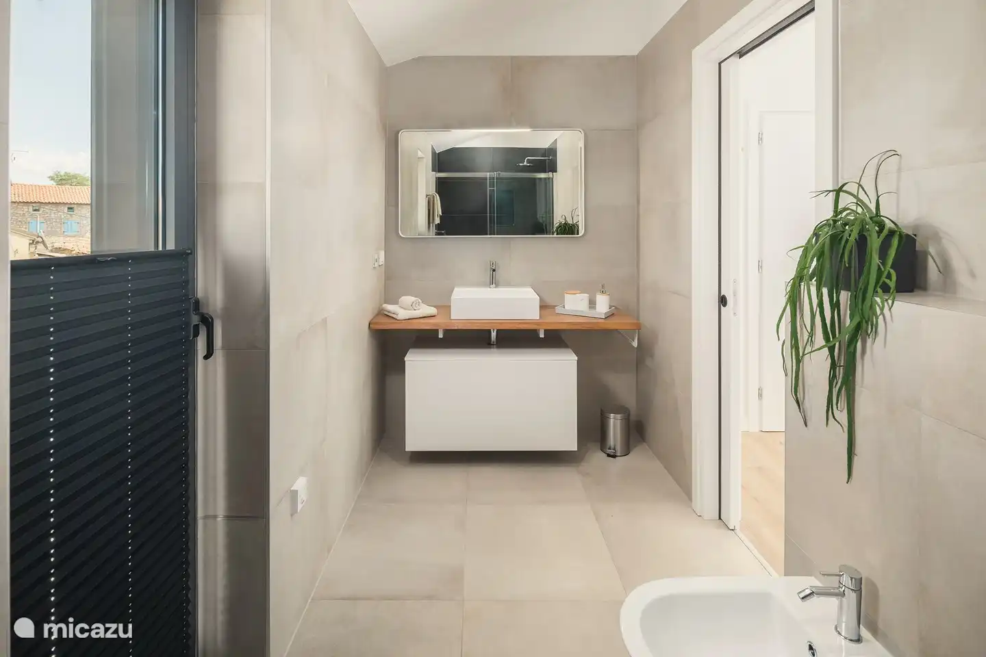 Badezimmer mit großzügiger ebenerdiger Dusche, WC, Bidet und Waschbecken.