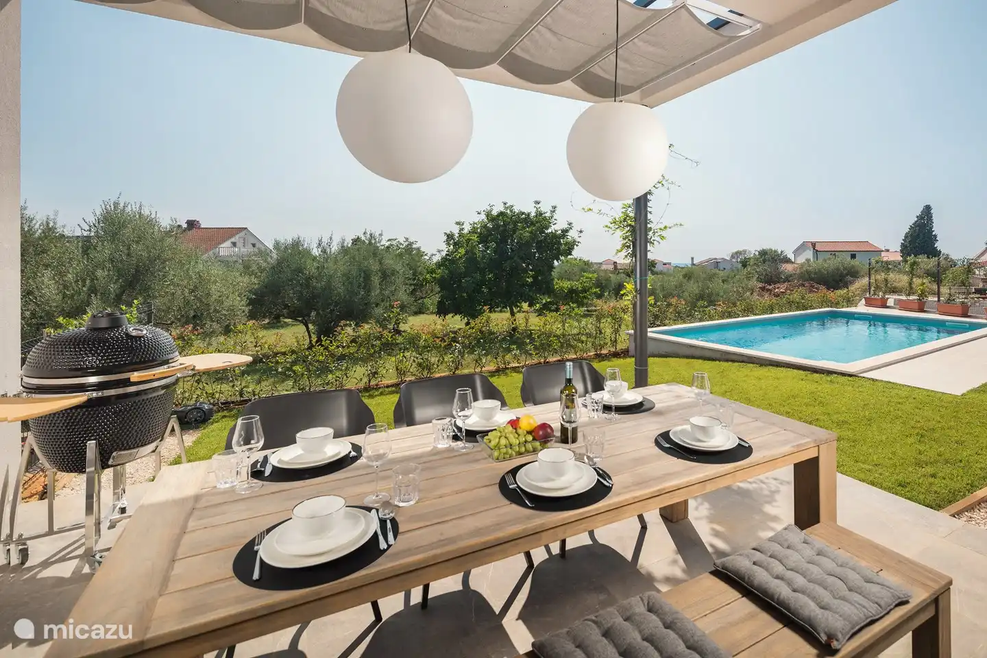 Überdachte Terrasse mit großem Esstisch und Grill.