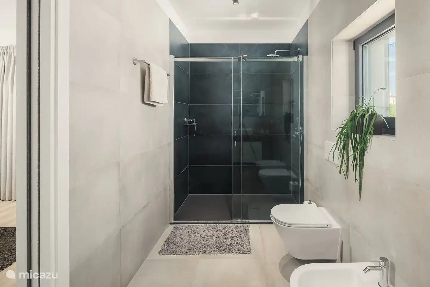 Badezimmer mit großzügiger ebenerdiger Dusche, WC, Bidet und Waschbecken.