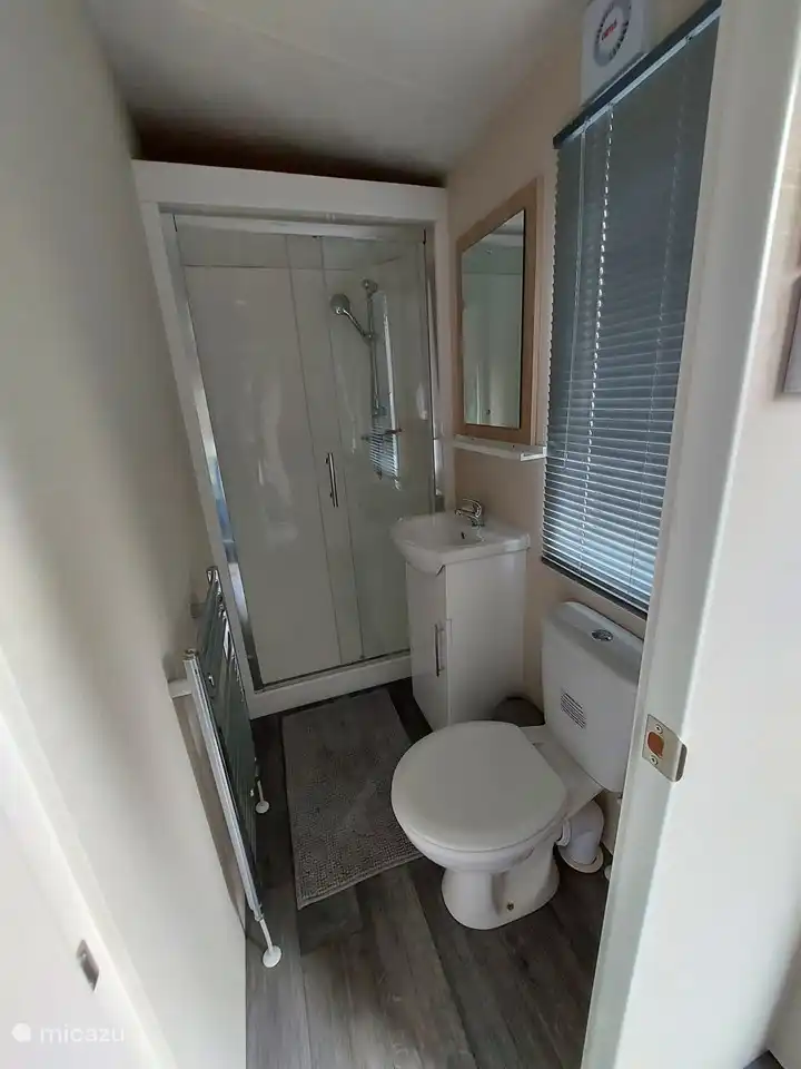 Badezimmer mit Dusche, Toilette und Waschbecken. Unter der Spüle befindet sich ein kleiner Schrank mit Stauraum.