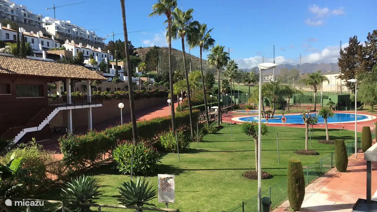 Blick von der hinteren Terrasse auf die Liegewiese, zwei Swimmingpools und das Clubhaus.
