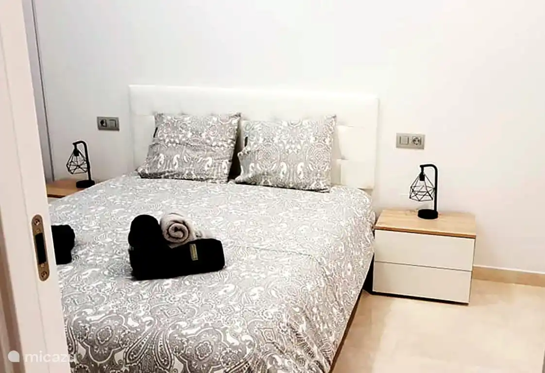 Schlafzimmer mit großen Schiebefenstern zur Terrasse. Großer Kleiderschrank mit Kleiderbügeln, außerdem zwei Nachttische mit Schubladen und Schuhregal.