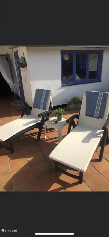 Die Terrasse mit Sonnenliegen, Fitnessgeräten, großem Sonnenschirm am Tisch und Bänken.