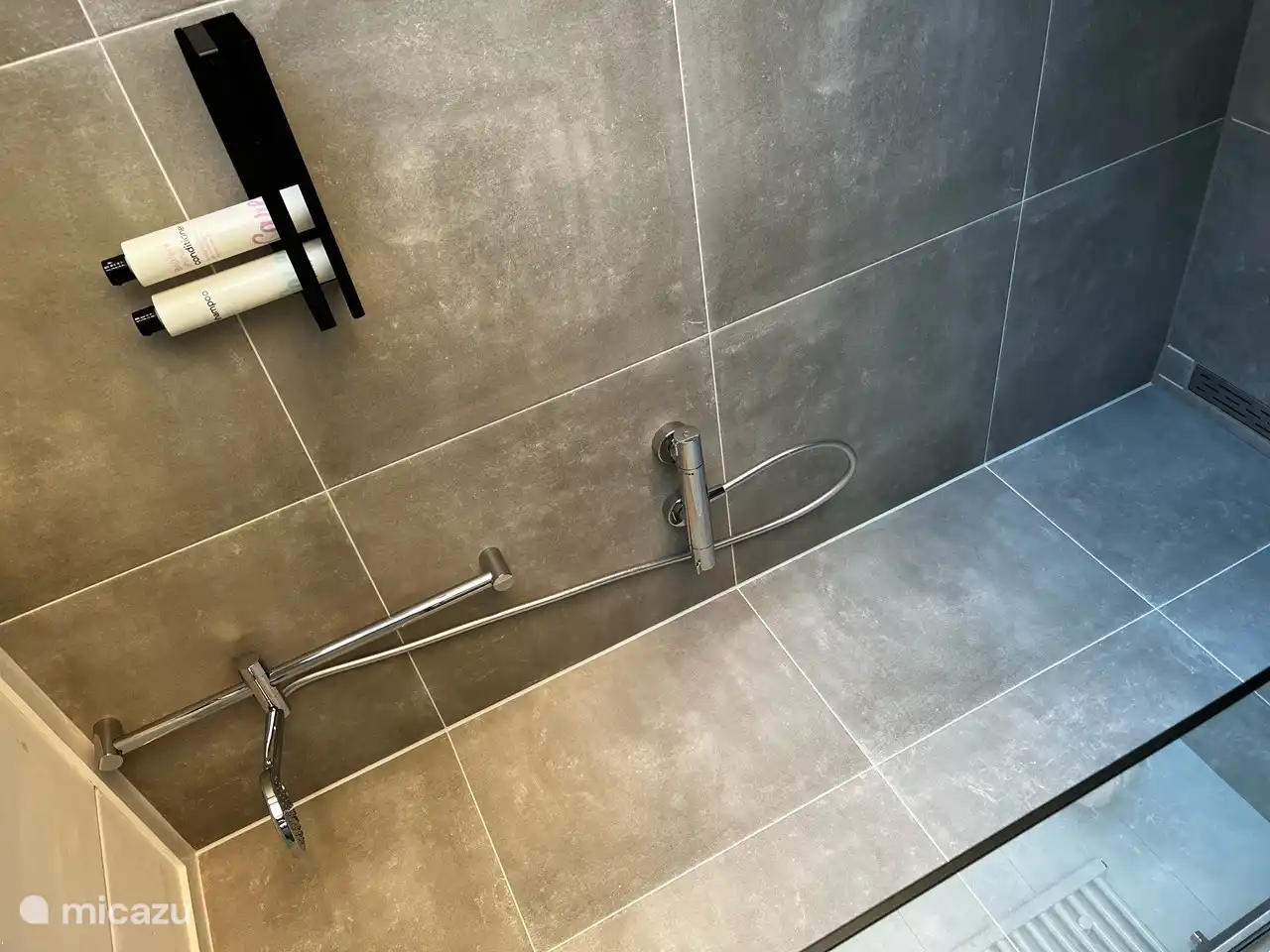 Die begehbare Dusche ist durch eine Glaswand vom Rest des Badezimmers getrennt.