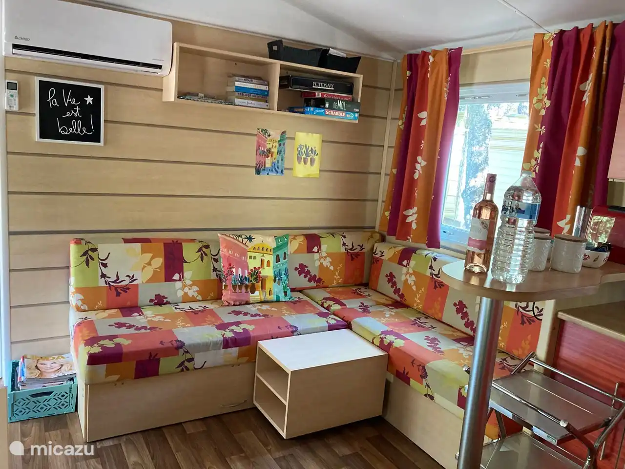 Vrolijk ingerichte woonkamer met open keuken. In de woonkamer hangt de airco voor een aangenaam verblijf in alle seizoenen. De kinderslaapkamer en het toilet bevinden zich links van de woonkamer, de ouderslaapkamer en de badkamer bevinden zich rechts van de woonkamer.
