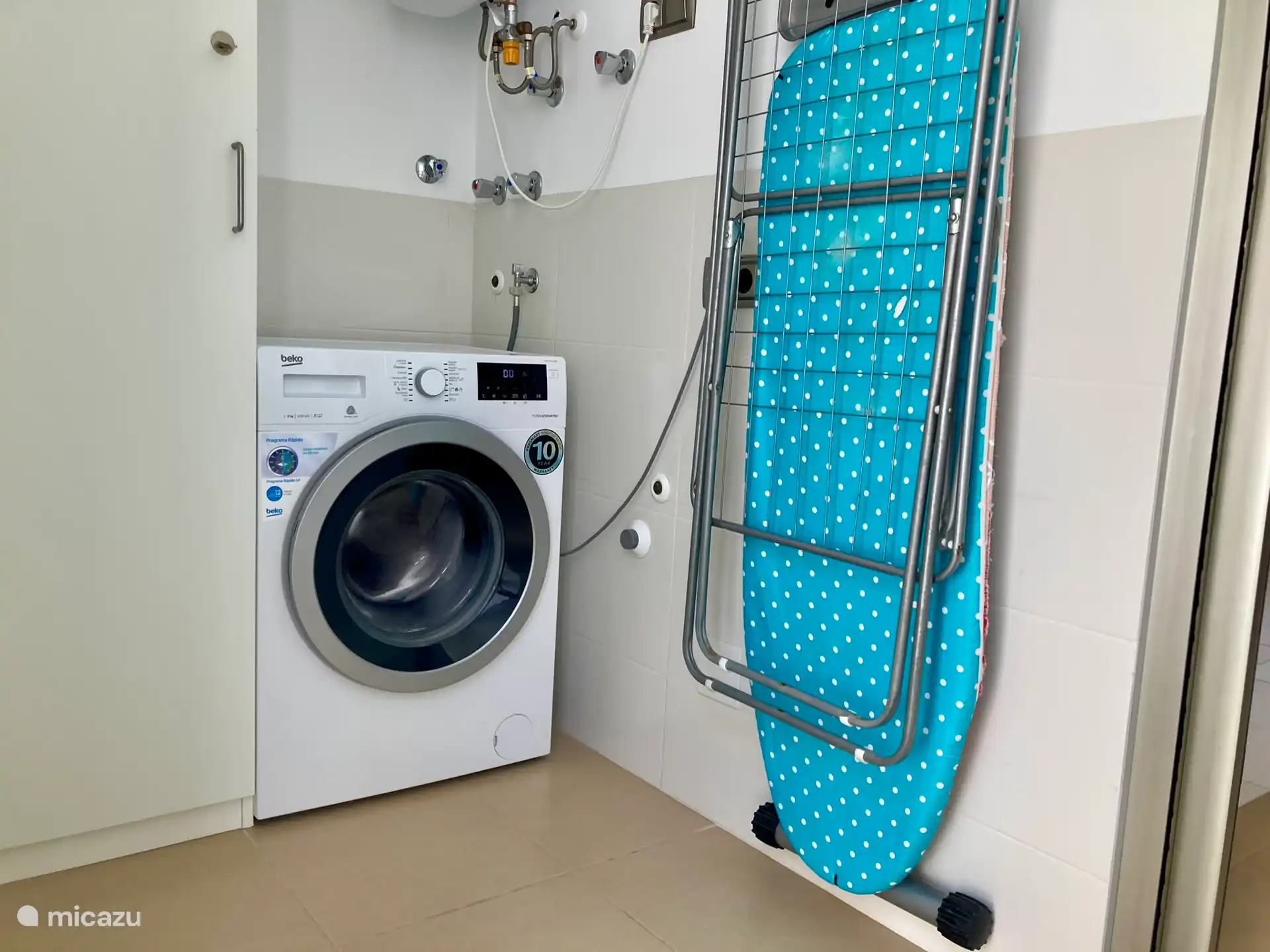 Storage room with a washing machine, drying rack and ironing board.