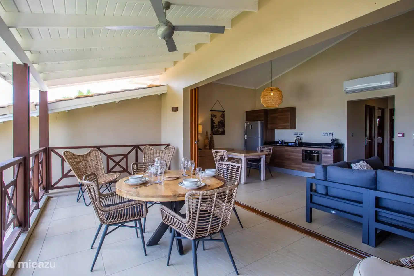 Balcón sombreado con mesa de comedor y puertas abiertas al área interior.