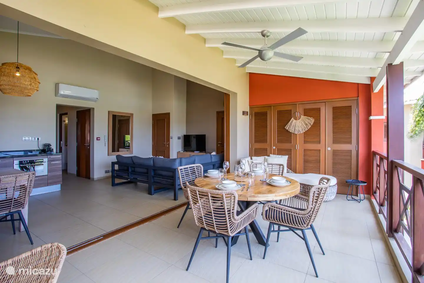 Balcón sombreado con mesa de comedor y puertas abiertas al área interior.