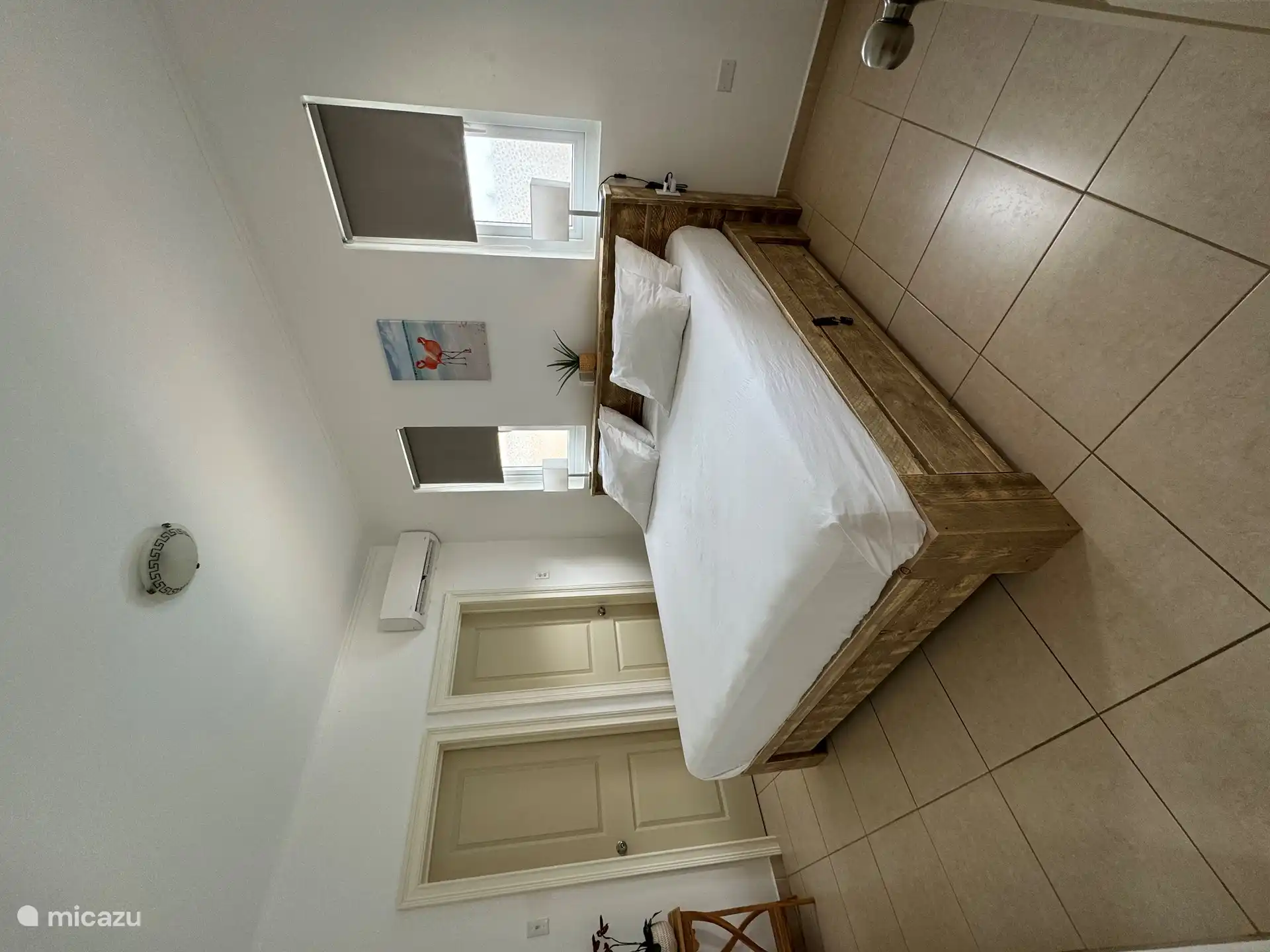 Grande chambre à l’arrière de la maison avec lit King-size, TV, passage vers un espace de rangement supplémentaire et une armoire et salle de bain privée.