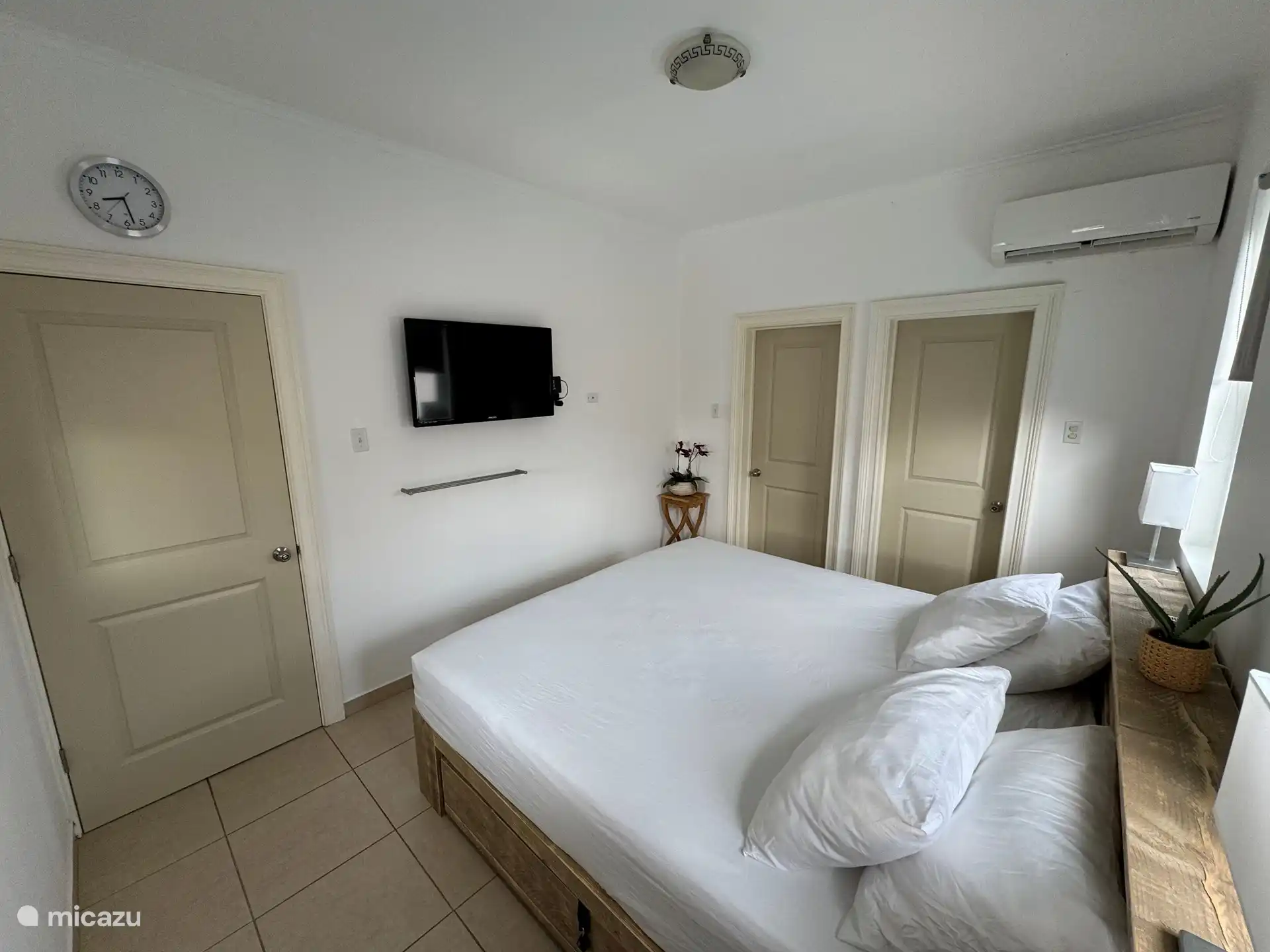 Grande chambre à l’arrière de la maison avec lit King-size, TV, passage vers un espace de rangement supplémentaire et une armoire et salle de bain privée.