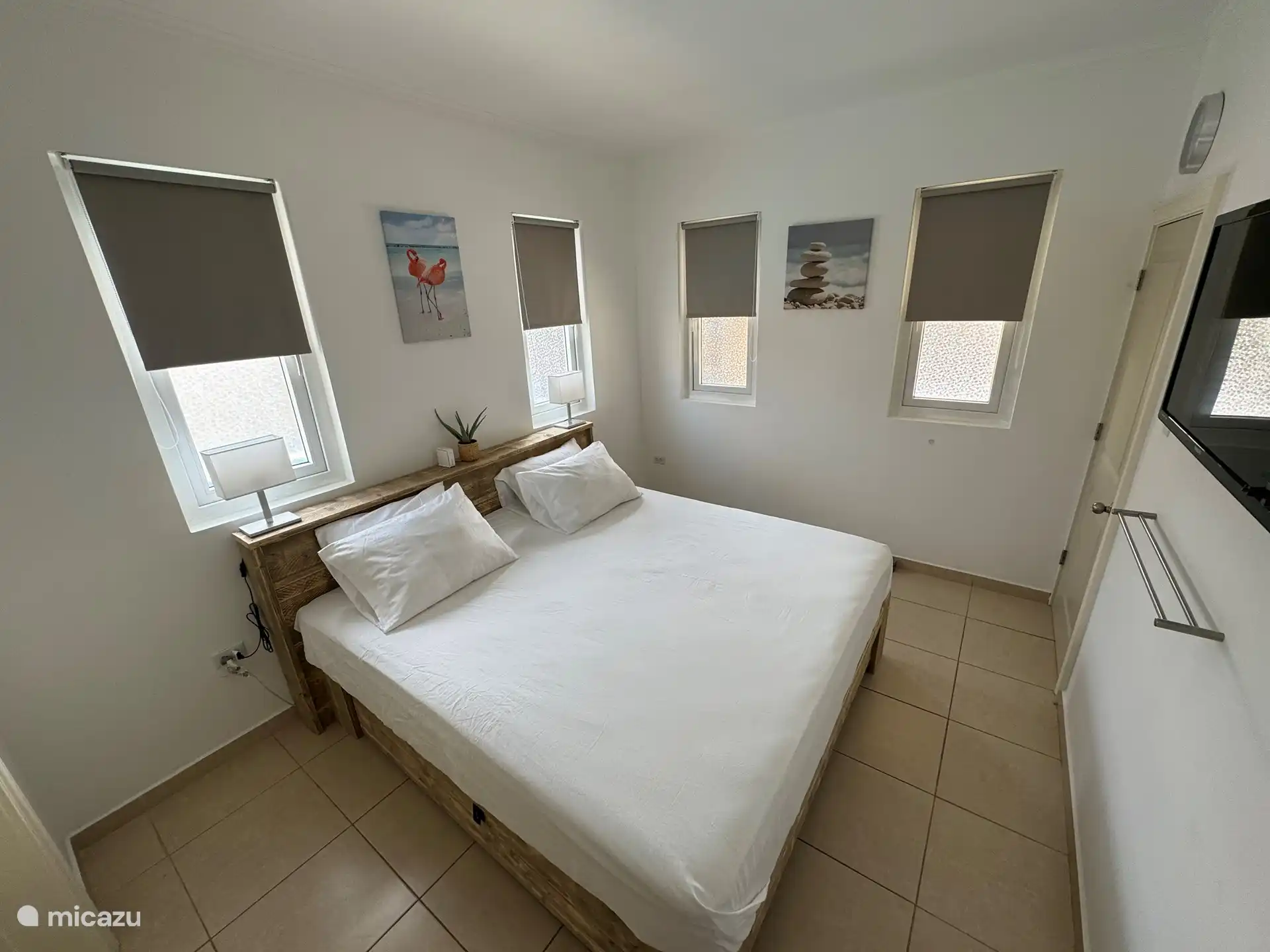 Grande chambre à l’arrière de la maison avec lit King-size, TV, passage vers un espace de rangement supplémentaire et une armoire et salle de bain privée.