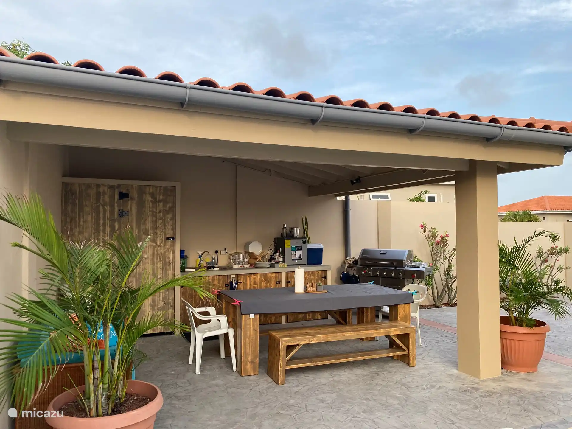 Cuisine extérieure entièrement équipée avec mini-réfrigérateur, barbecue, table à manger avec bancs et canapé séparé sous Cazebo.