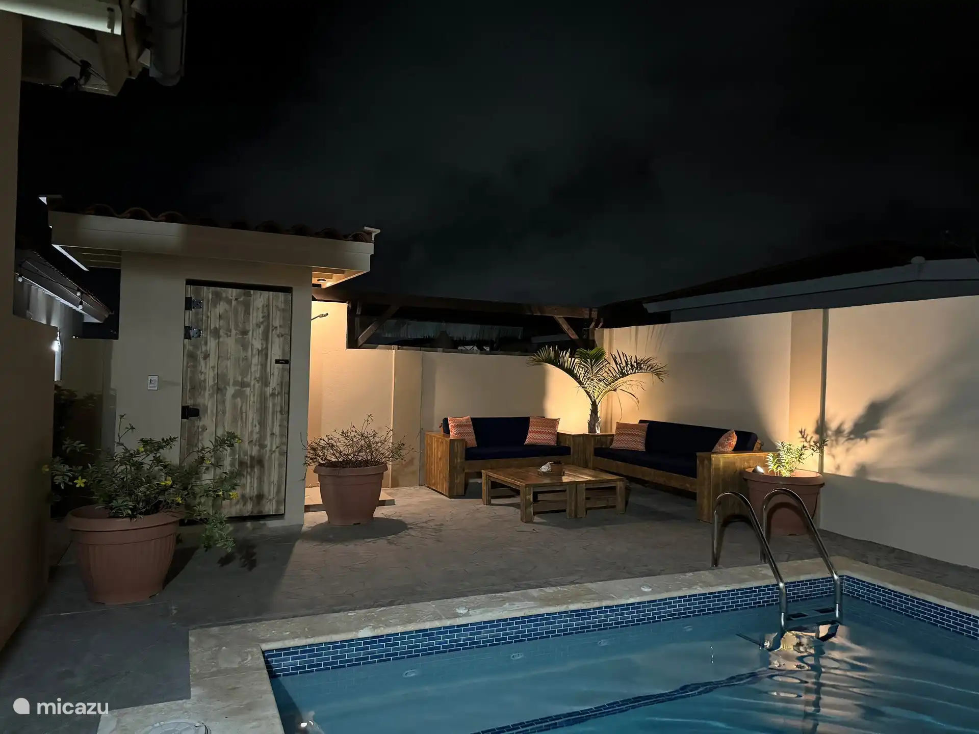 Vue sur coin détente avec WC extérieur et douche depuis la piscine.