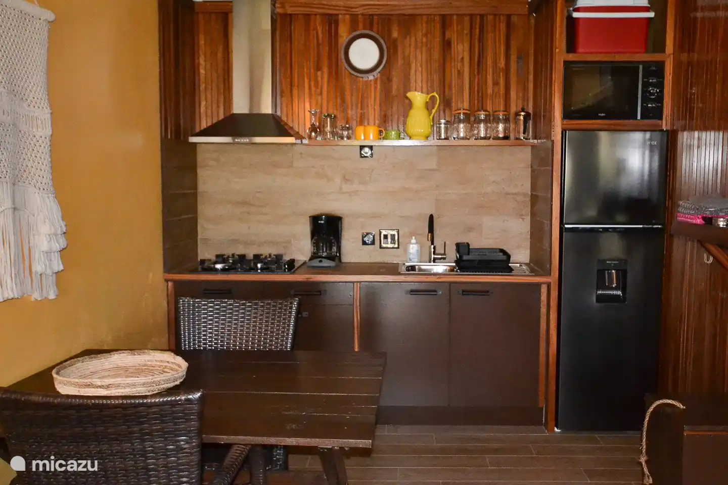 Voll ausgestattete (offene) Küche mit Herd, Dunstabzugshaube, Kühlschrank mit Gefrierfach und Kaltwasserhahn, Mikrowelle, Kaffeemaschine, Wasserkocher.